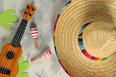 Photo of Mexican sombrero hat, ukulele and maracas on grey textured table, flat lay