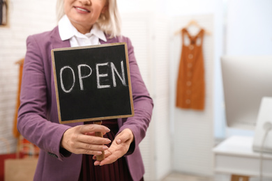Photo of Female business owner holding OPEN sign in boutique, closeup