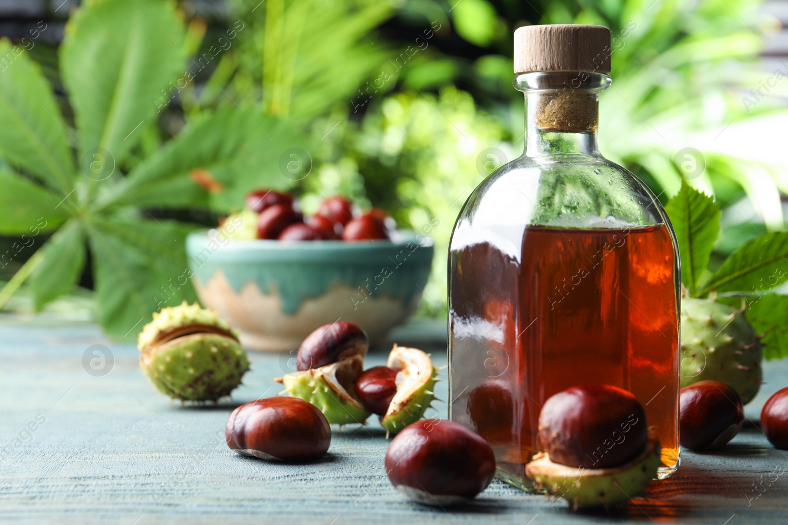 Photo of Chestnuts and bottle of essential oil on table against blurred background. Space for text