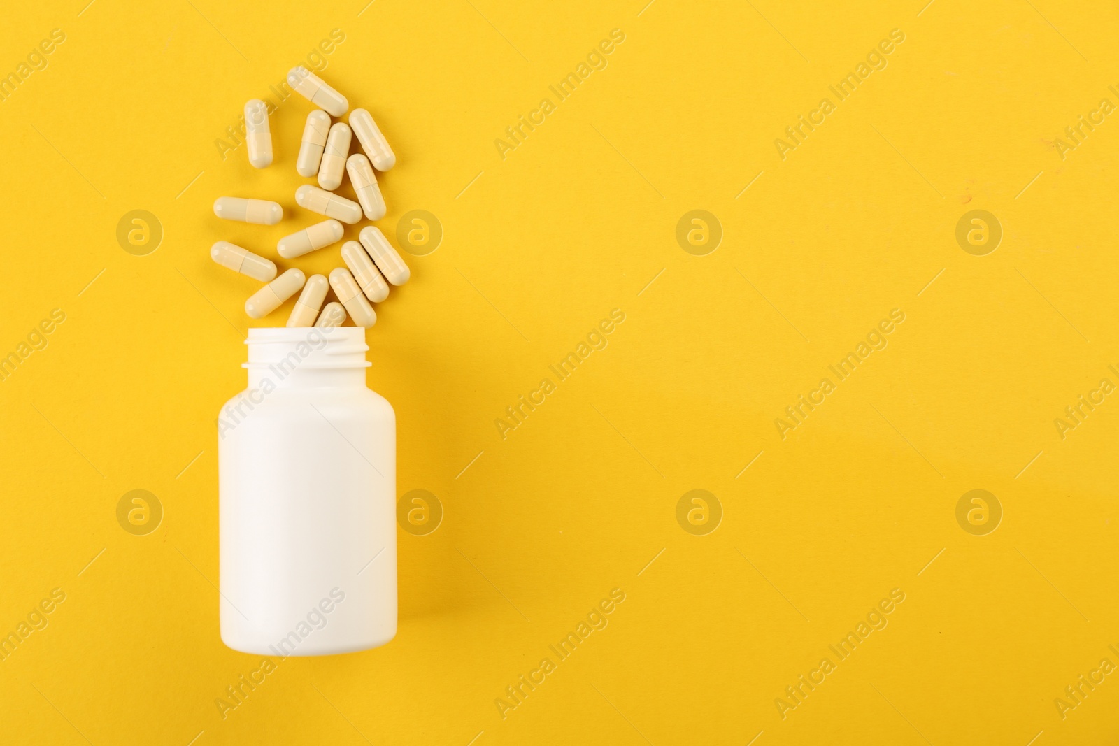 Photo of Bottle and vitamin capsules on yellow background, top view. Space for text