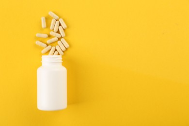 Photo of Bottle and vitamin capsules on yellow background, top view. Space for text