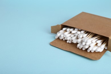 Box with wooden cotton buds on light blue background. Space for text