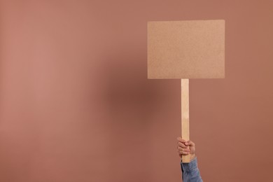Man holding blank sign on brown background, closeup. Space for text