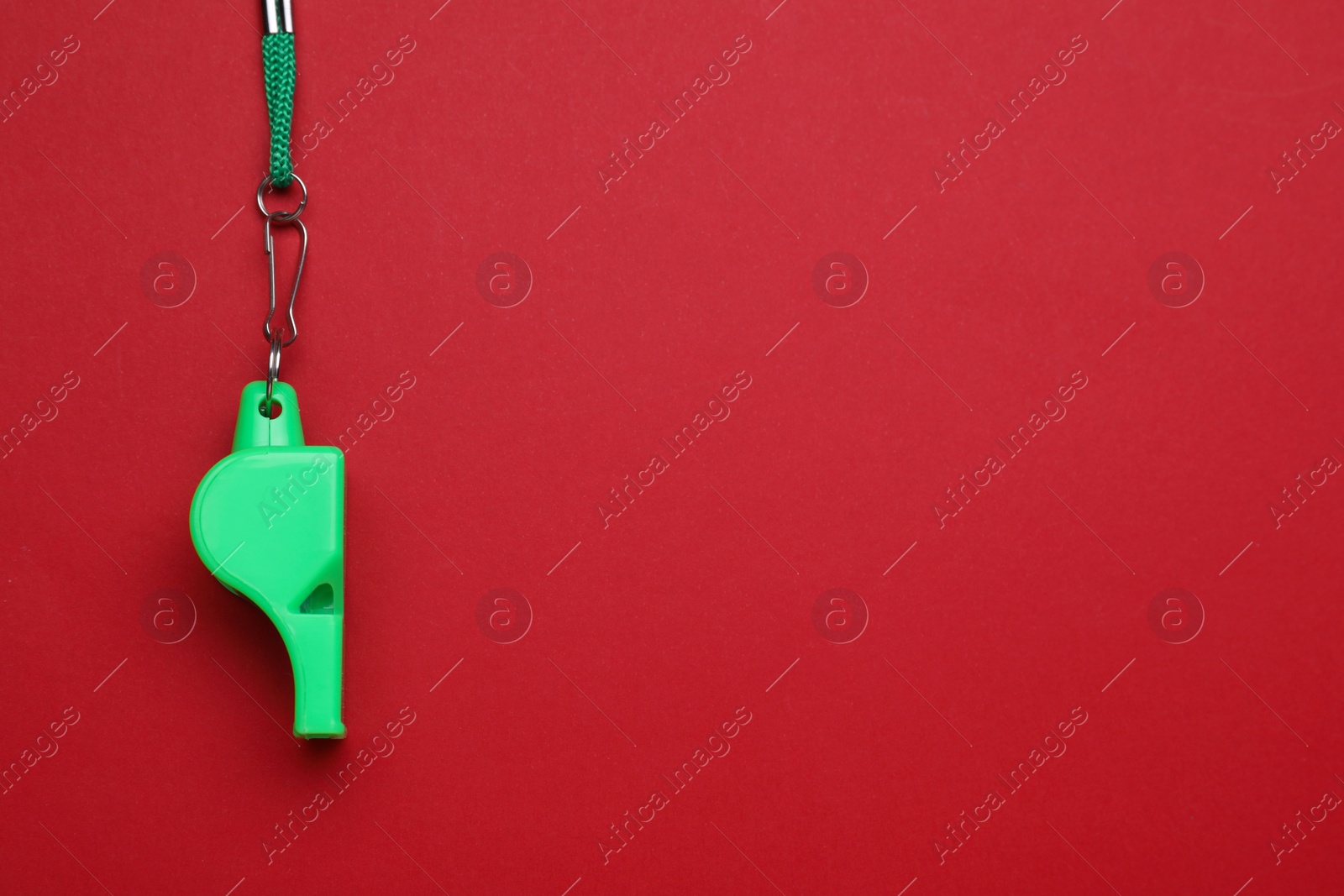 Photo of One green whistle with cord on red background, top view. Space for text