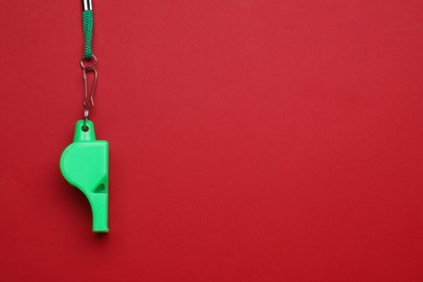 Photo of One green whistle with cord on red background, top view. Space for text