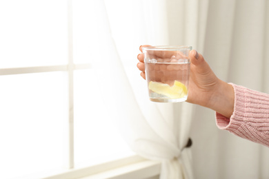 Photo of Woman with tasty lemon water near window, closeup