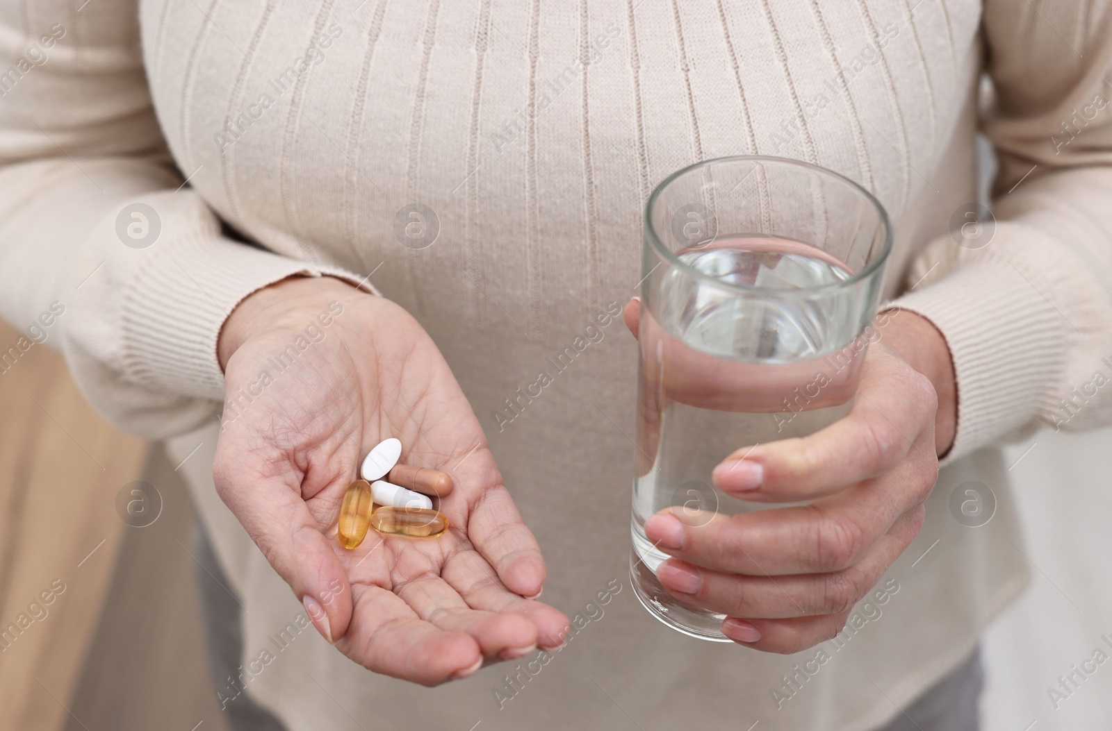 Photo of Woman with vitamin pills and glass of water indoors, closeup