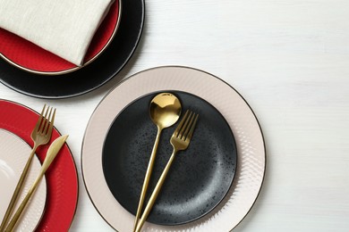 Stylish ceramic plates, cutlery and napkin on white wooden table, flat lay