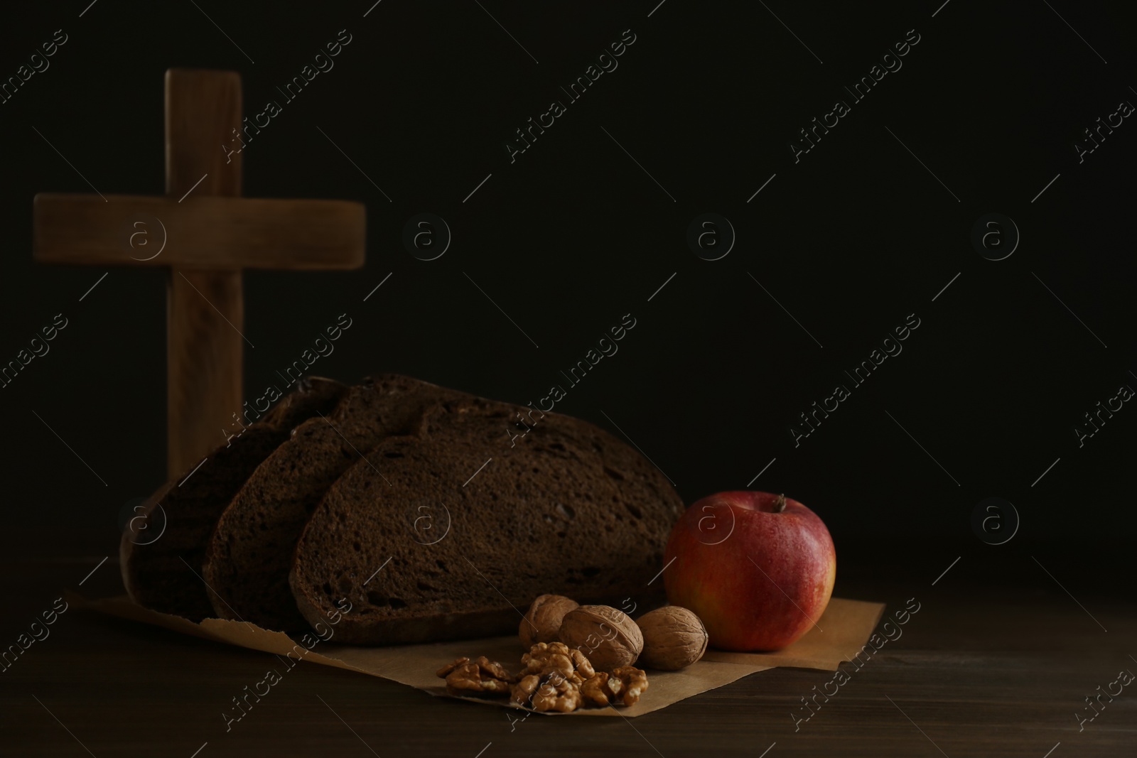 Photo of Bread, apple, walnuts and cross on wooden table, space for text. Great Lent season