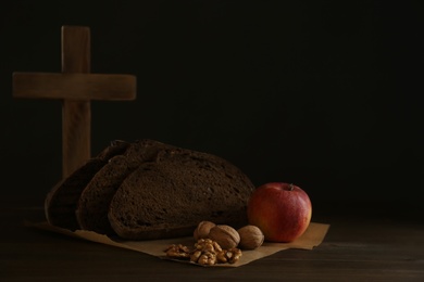Photo of Bread, apple, walnuts and cross on wooden table, space for text. Great Lent season
