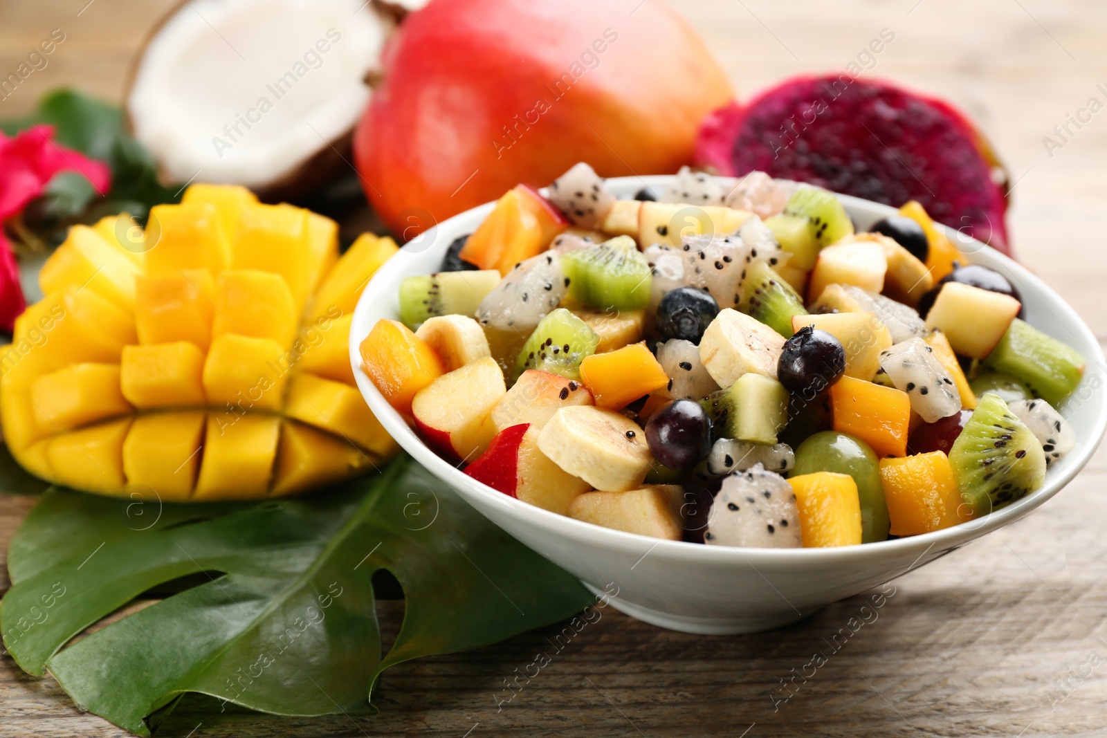 Photo of Delicious exotic fruit salad and ingredients on wooden table