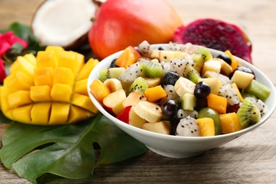 Photo of Delicious exotic fruit salad and ingredients on wooden table