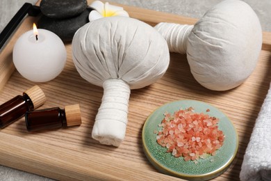Photo of Wooden tray with herbal massage bags, essential oils, sea salt, spa stones and candle on grey table, closeup