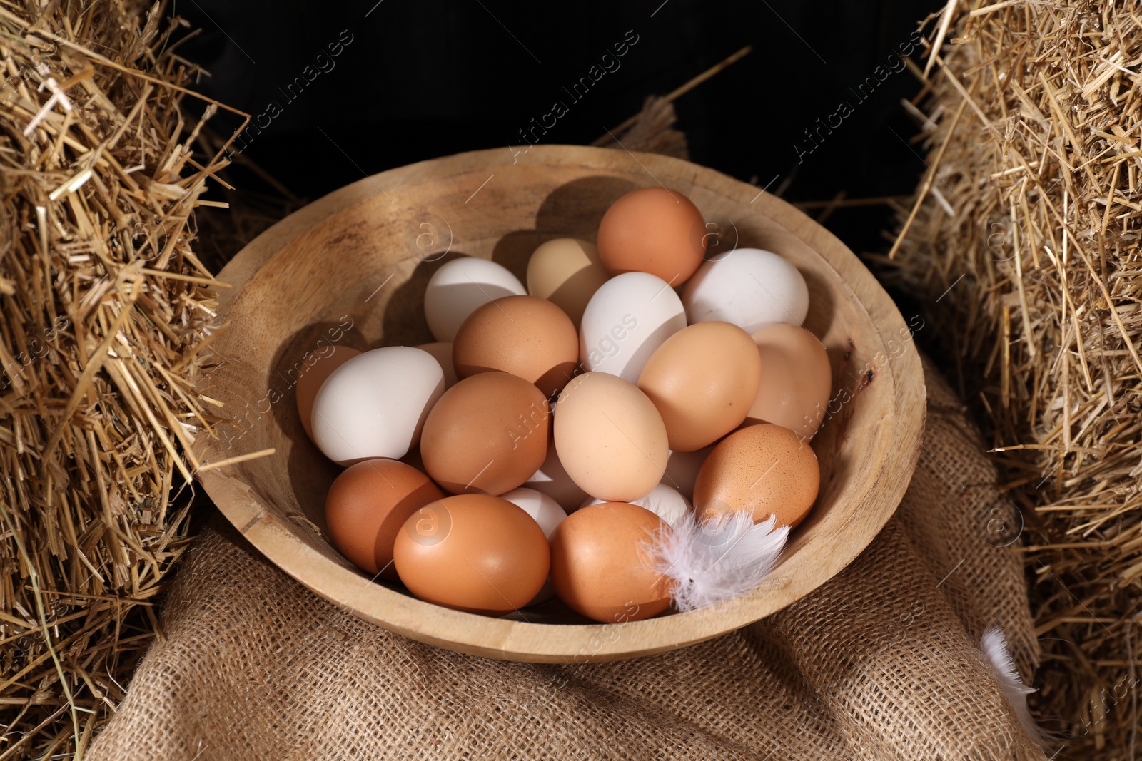 Photo of Fresh chicken eggs in bowl among dried straw bales