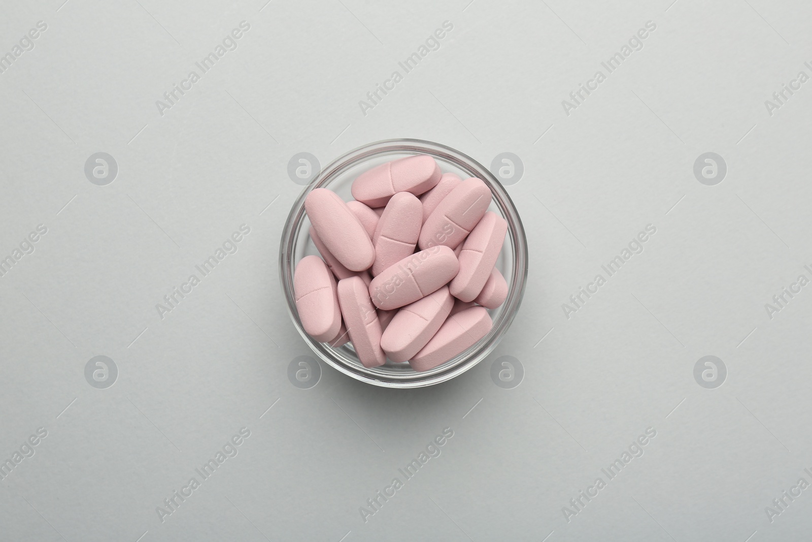 Photo of Vitamin pills in bowl on grey background, top view