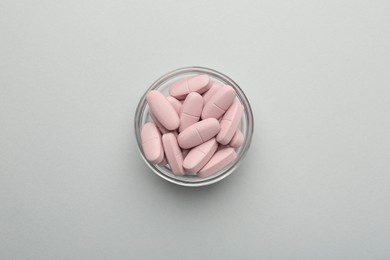 Photo of Vitamin pills in bowl on grey background, top view