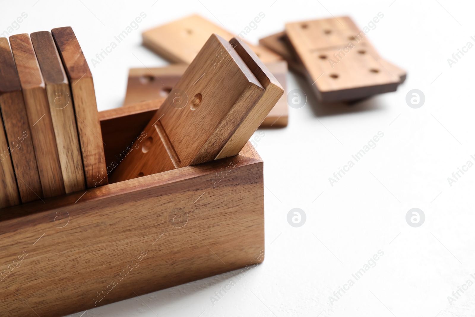 Photo of Set of wooden dominoes in box on white table, closeup