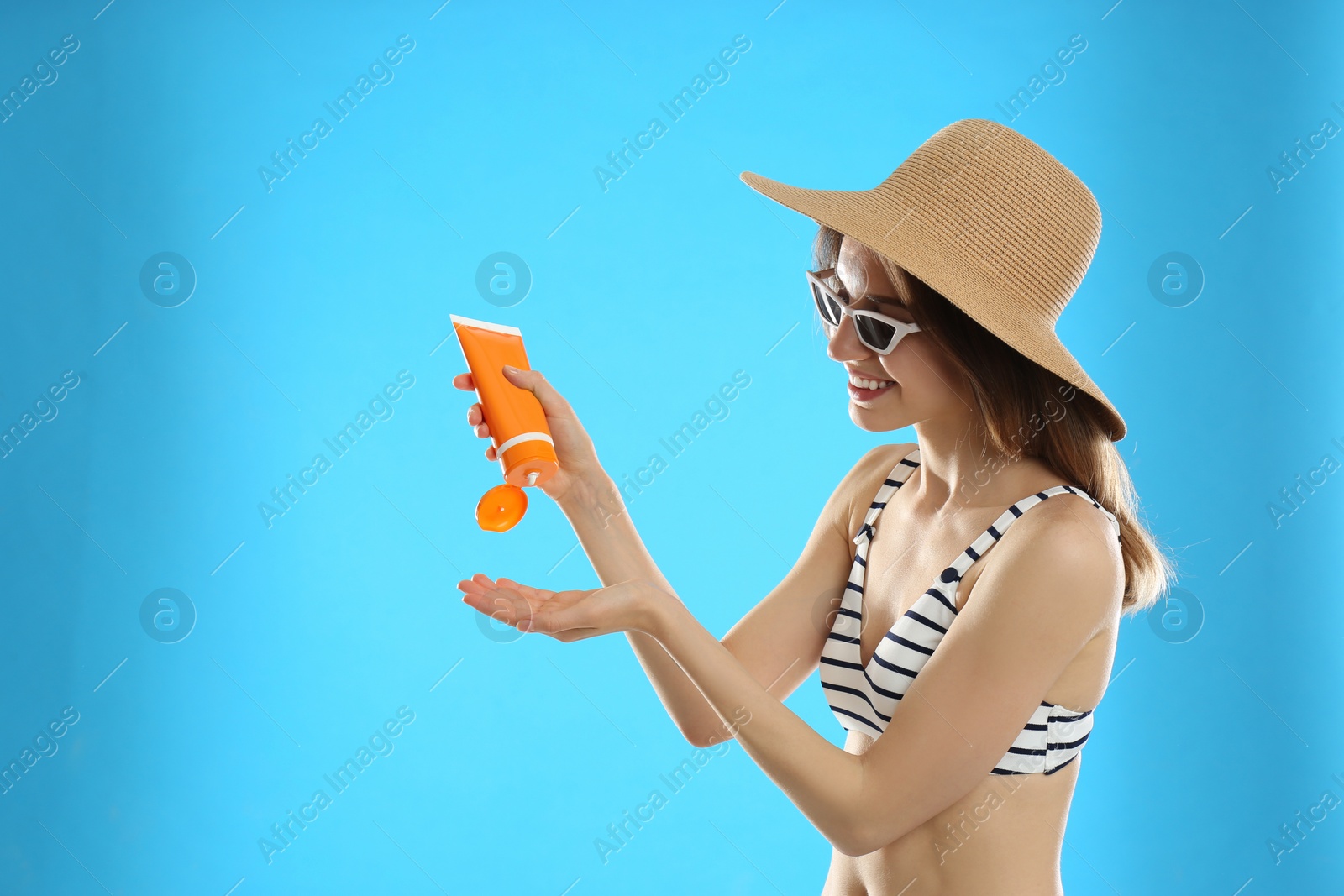 Photo of Young woman applying sun protection cream on light blue background