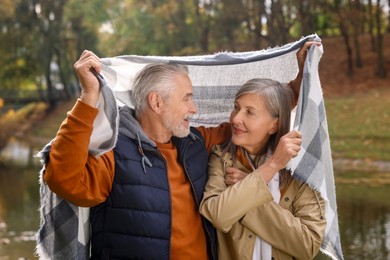 Photo of Affectionate senior couple under blanket in autumn park