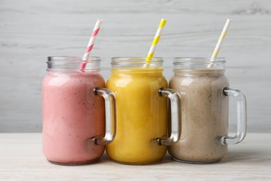 Photo of Mason jars with different tasty smoothies on white wooden table