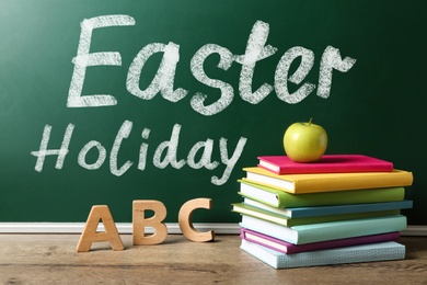 Image of Text Easter Holiday on green chalkboard near wooden table. School break 