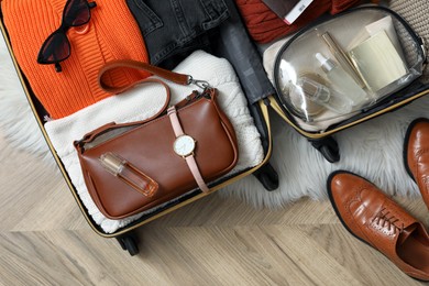 Photo of Open suitcase with folded clothes, accessories and shoes on floor, flat lay