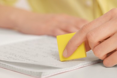 Photo of Girl erasing mistake in her notebook at white desk, closeup