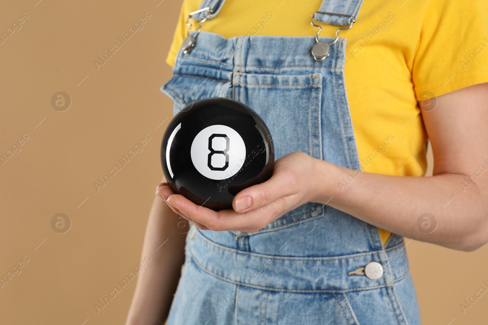 Photo of Woman holding magic eight ball on light brown background, closeup