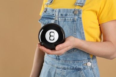 Woman holding magic eight ball on light brown background, closeup