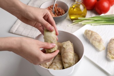 Photo of Woman putting uncooked stuffed cabbage roll into ceramic pot at white table, closeup