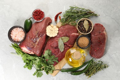 Photo of Pieces of raw beef meat, herbs and spices on light grey marble table, flat lay