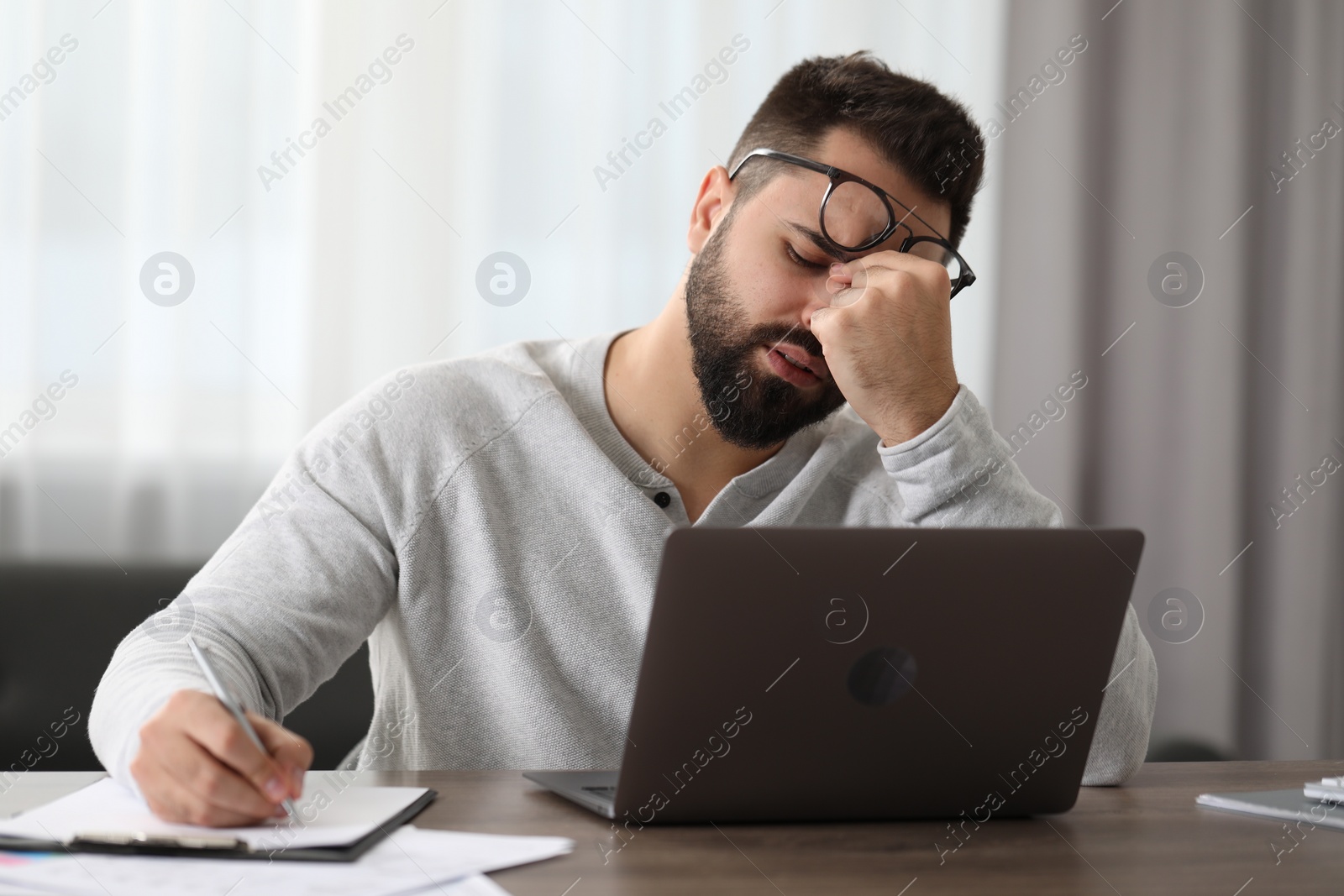 Photo of Man with glasses suffering from headache at workplace in office