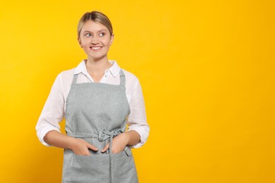 Photo of Beautiful young woman in clean apron with pattern on orange background. Space for text