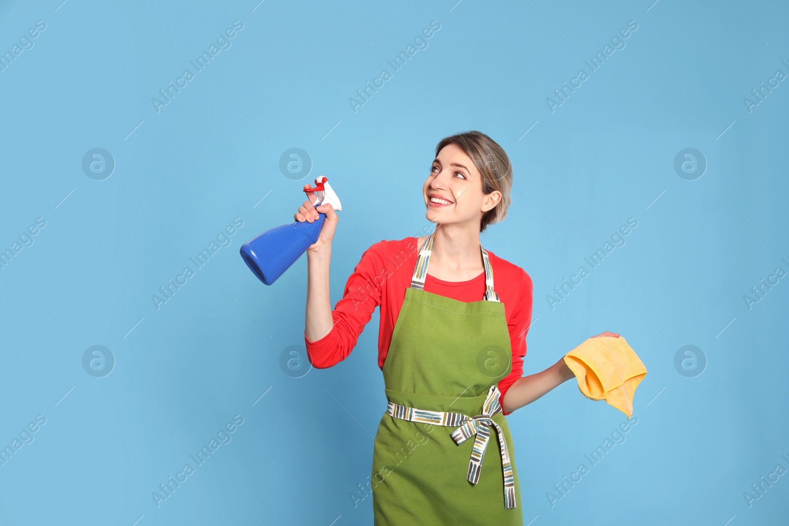 Photo of Young housewife with detergent and rag on light blue background