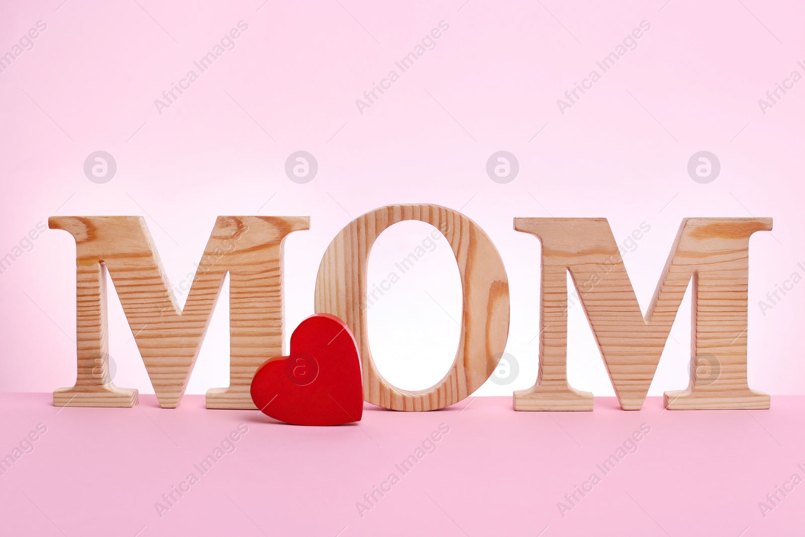 Photo of Word MOM made of wooden letters and small red heart for Mother's Day on color background