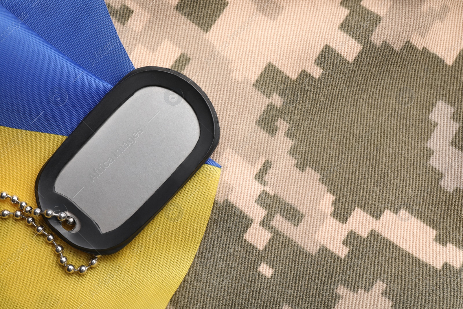 Photo of Military ID tag and Ukrainian flag on pixel camouflage, flat lay. Space for text