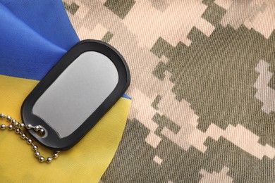 Military ID tag and Ukrainian flag on pixel camouflage, flat lay. Space for text