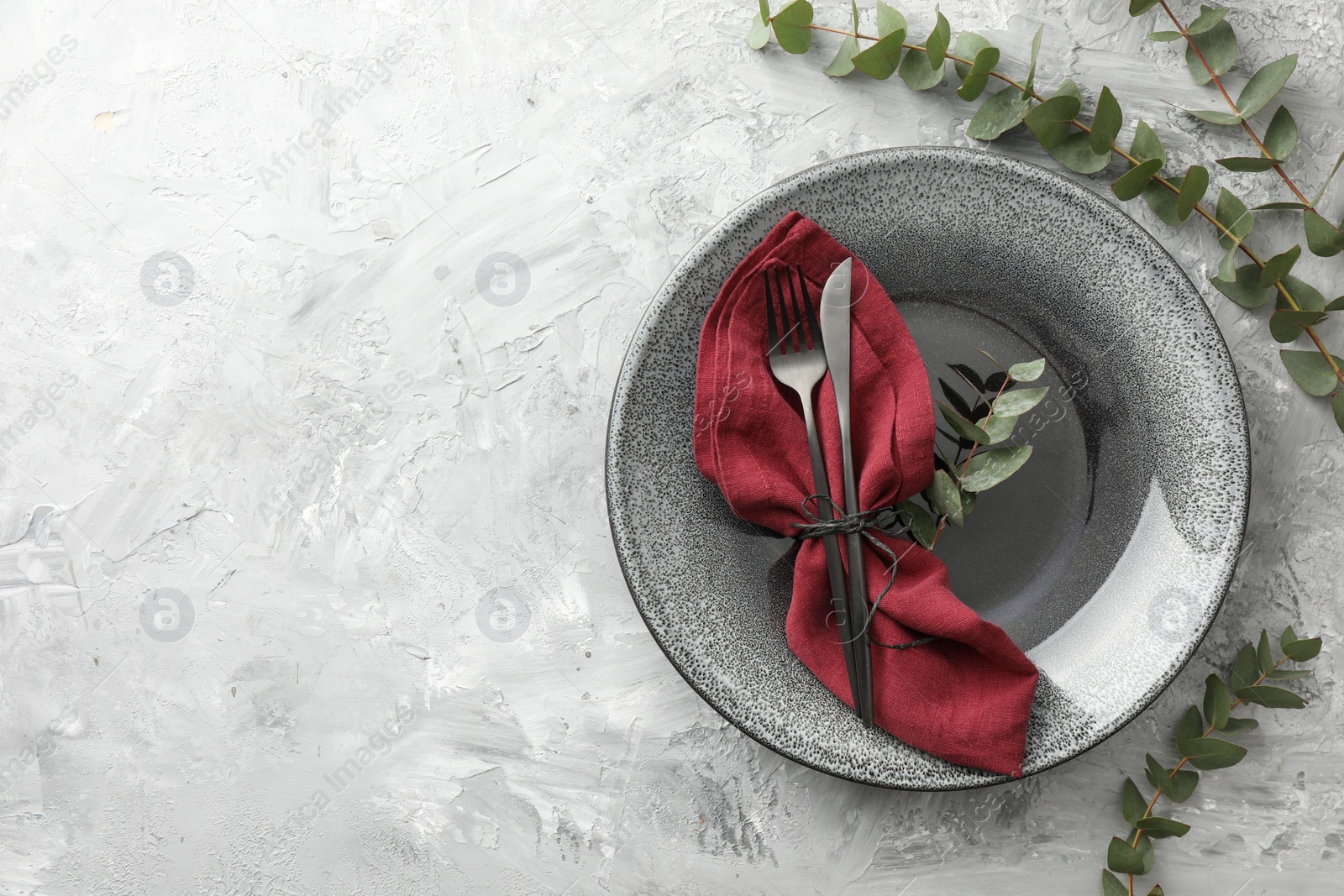 Photo of Stylish setting with cutlery, napkin, eucalyptus branches and plate on grey textured table, top view. Space for text