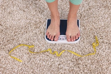 Photo of Woman standing on floor scale and measuring tape on carpet, closeup