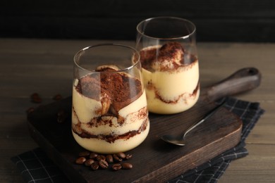 Delicious tiramisu in glasses, spoon and coffee beans on wooden table, closeup