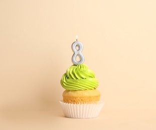 Birthday cupcake with number eight candle on beige background