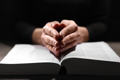 Photo of Religion. Christian woman praying over Bible at table, closeup