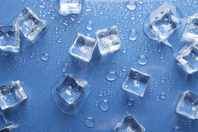Melting ice cubes and water drops on blue background, flat lay
