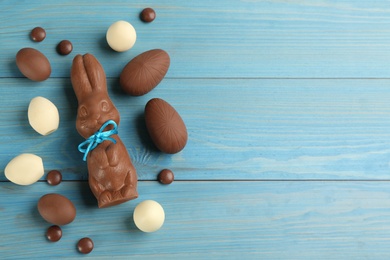 Chocolate Easter bunny, candies and eggs on light blue wooden table, flat lay. Space for text