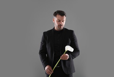Photo of Sad man with calla lily flower on grey background. Funeral ceremony