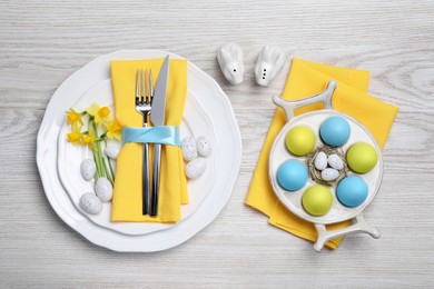 Festive table setting with painted eggs and cutlery on white wooden background, flat lay. Easter celebration