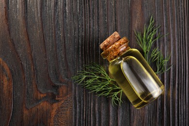 Bottle of essential oil and fresh dill on dark wooden table, flat lay. Space for text