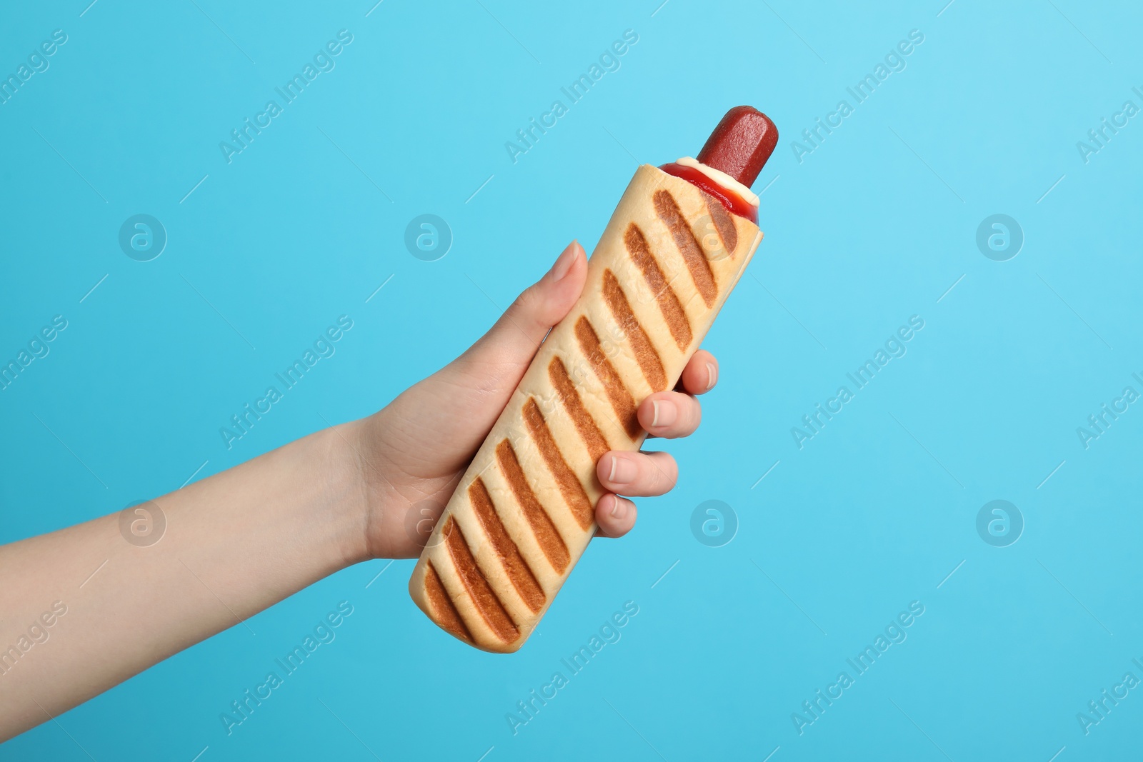 Photo of Woman holding delicious french hot dog on light blue background, closeup