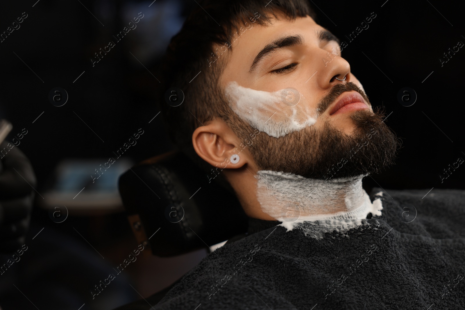 Photo of Bearded client with shaving foam on face in barbershop, closeup