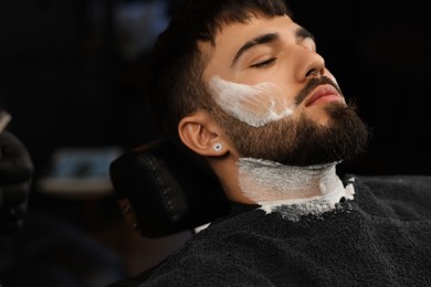 Photo of Bearded client with shaving foam on face in barbershop, closeup